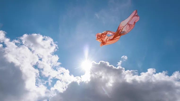 A piece of pink, translucent fabric floating in the sky against bright sunlight and white clouds